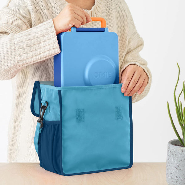Lunchbag OmieTote – Blue mit blauer Lunchbox wird von Person in weißem Pullover gehalten