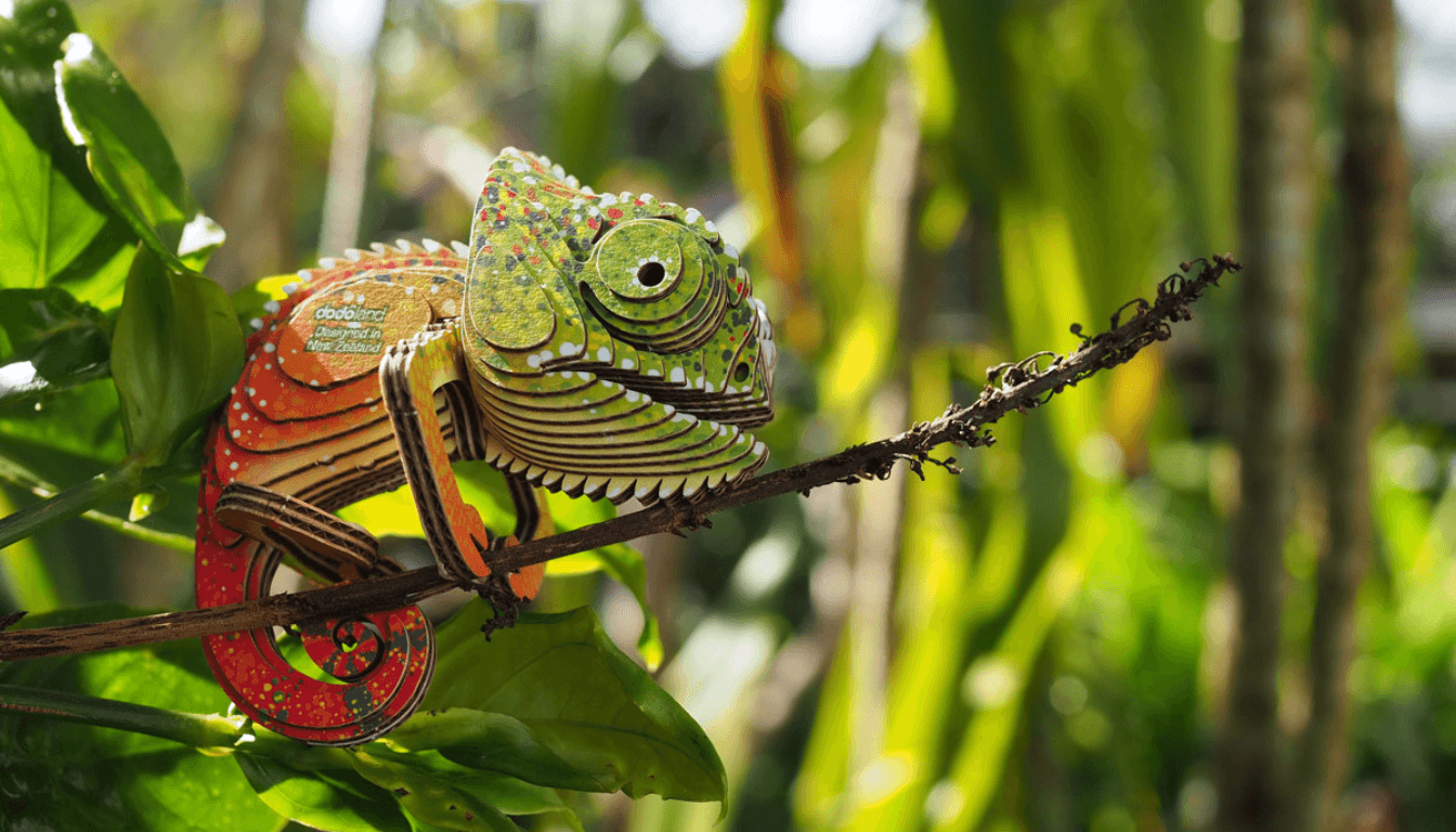 Eugy Figuren für Kinder: farbenfrohes Chamäleon aus Karton auf einem Ast in einem grünen Garten
