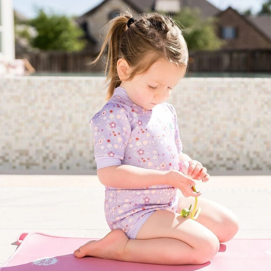 Kleines Mädchen in UV-Badebekleidung sitzt auf Matte mit Spielzeug für Strand & Pool