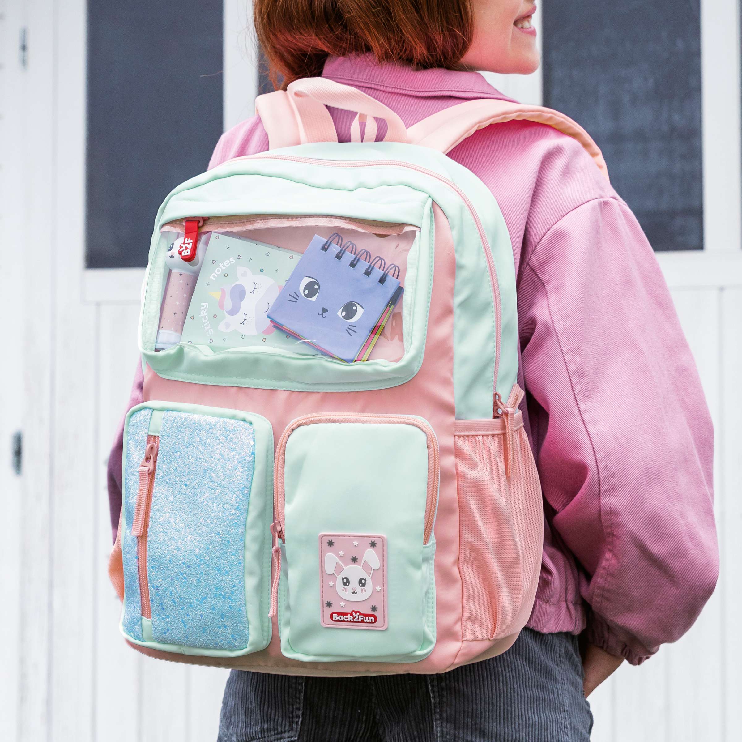 Bunter Schulranzen mit mehreren Taschen und transparentem Fach getragen von Kind im rosa Pullover Schulranzen & Schulrucksäcke