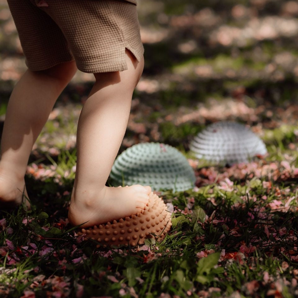 Kind balanciert barfuß auf taktilen Spielgeräten im Garten beim draußen spielen