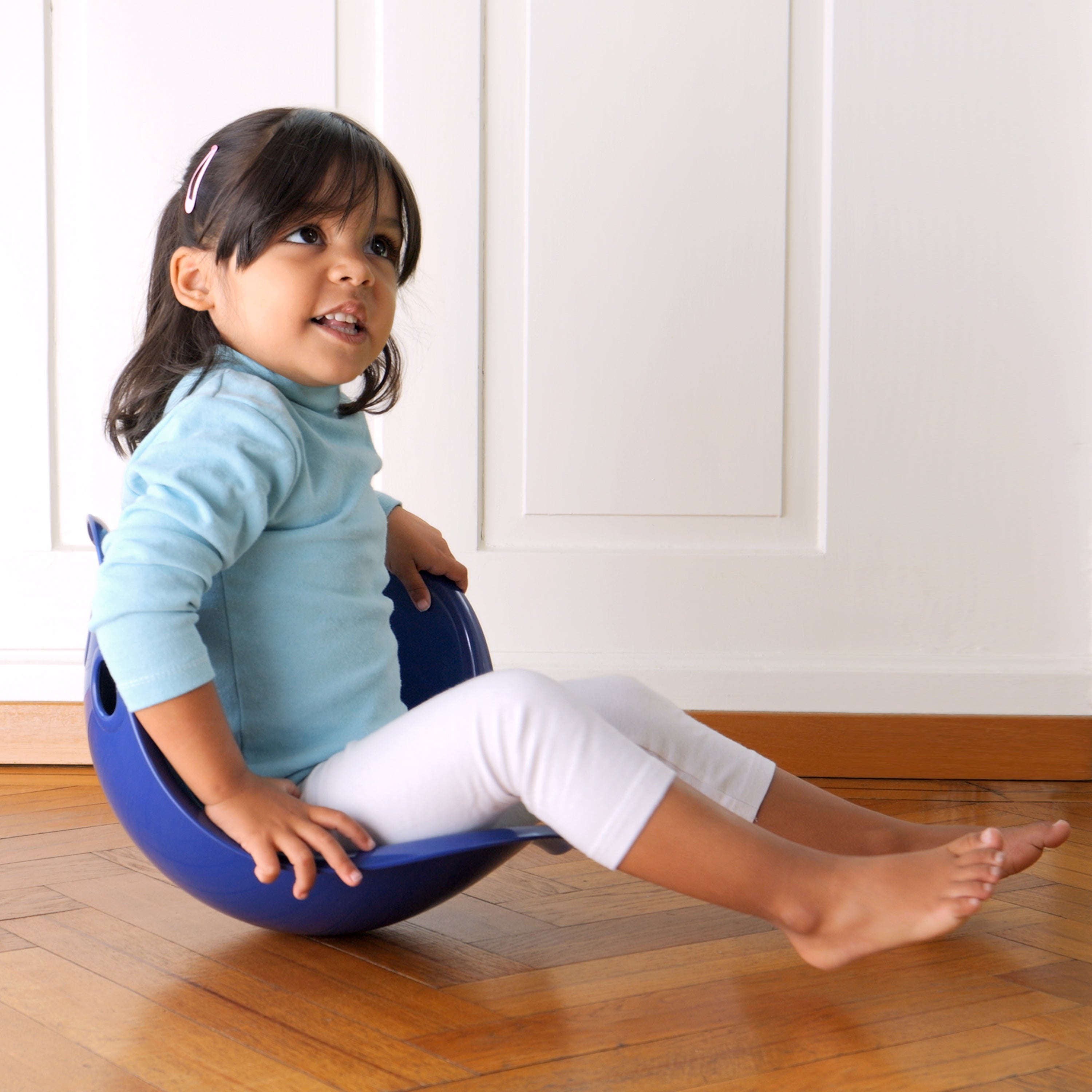 Kleines Mädchen spielt kreativ mit rundem Sitzspielzeug auf Holzboden kreatives Spielzeug