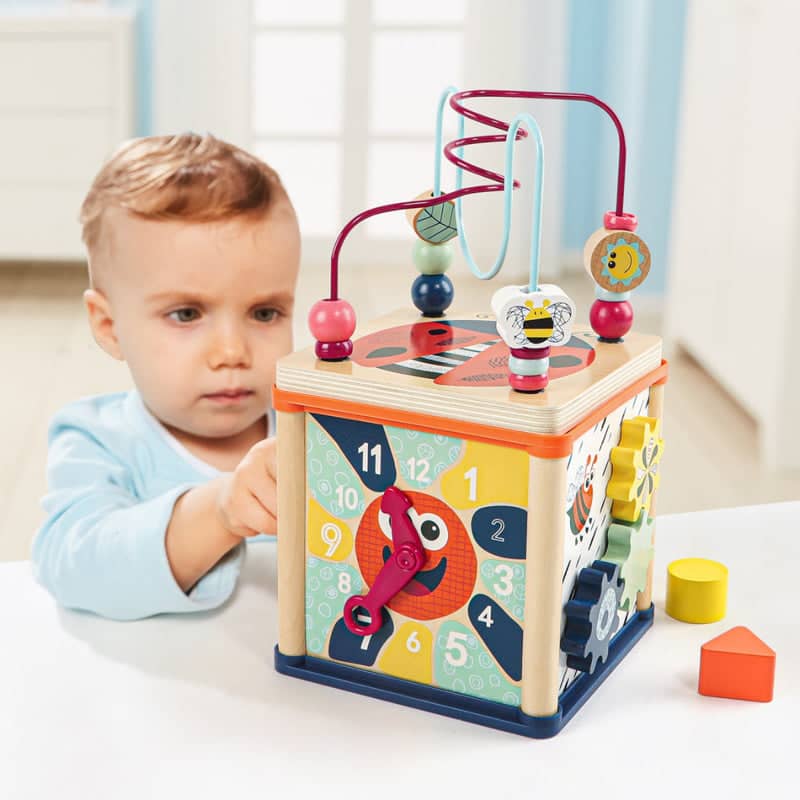 Kleinkind spielt mit buntem Lernwürfel mit Uhr, Labyrinth und Sortierformen im Kinderzimmer Lerntische und Lernwürfel