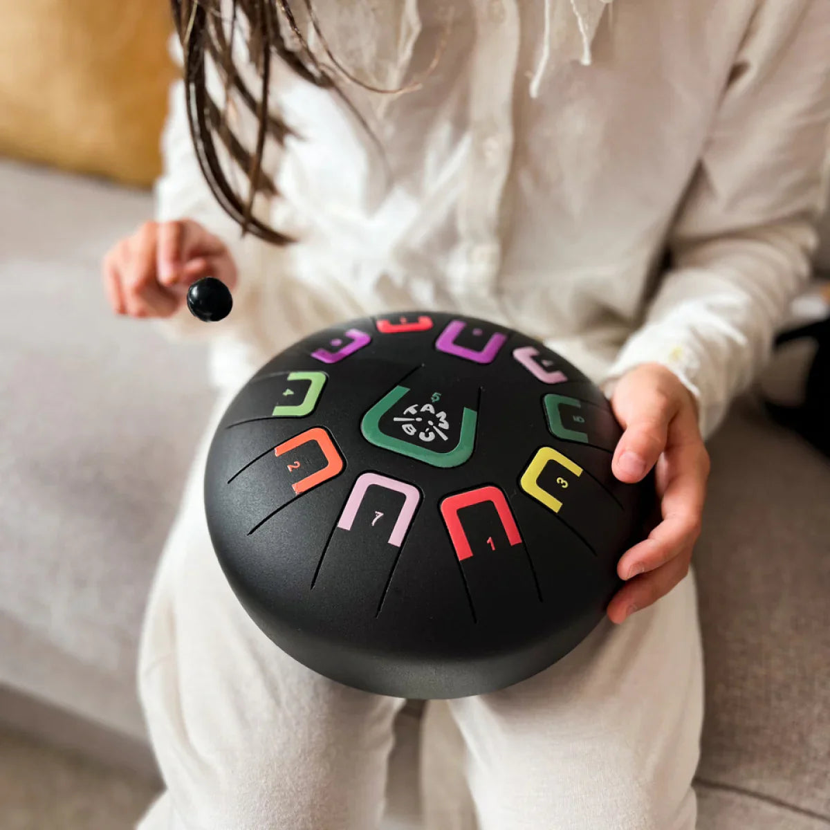 Kind spielt mit buntem Musikinstrument aus Metall mit Schlägel auf dem Schoß sitzend