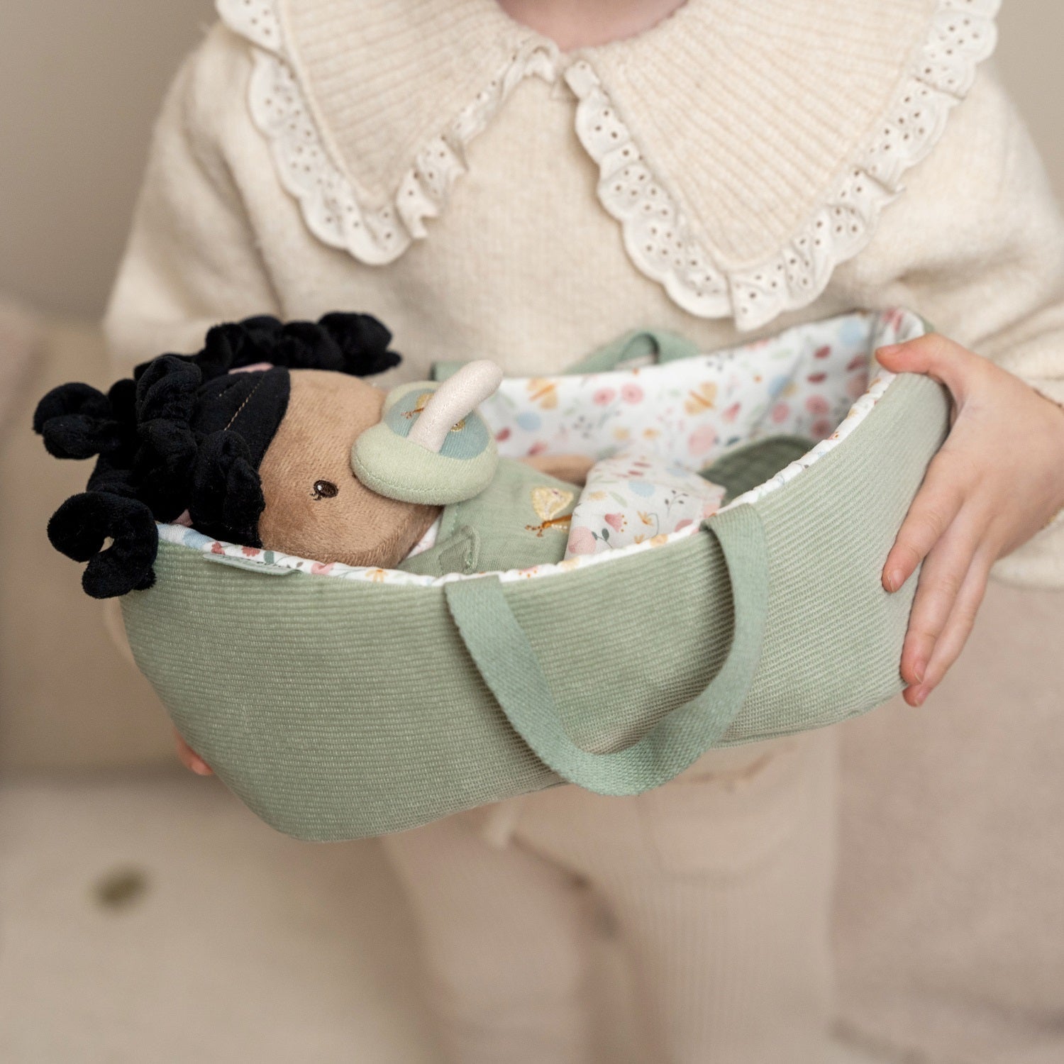 Kind hält eine Stoffpuppe in einer Stoffwiege aus der Kollektion Puppen und Zubehör