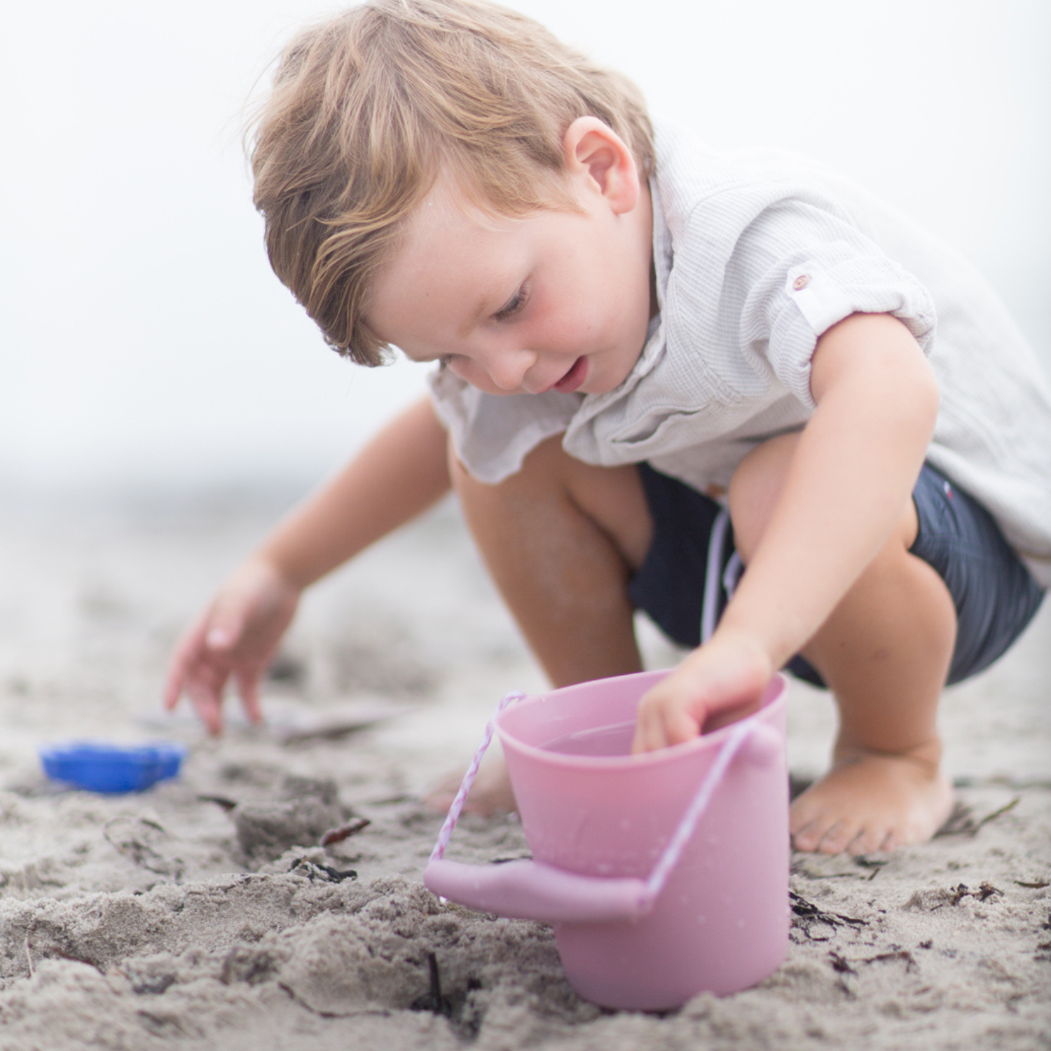 Kleiner Junge spielt konzentriert mit Sandspielzeug Eimer und Förmchen im Sand am Strand