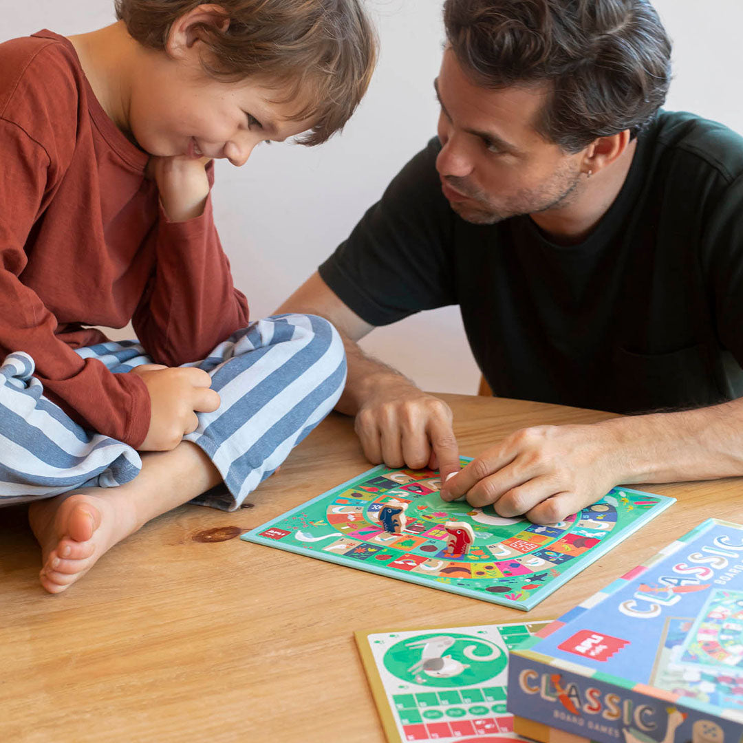 Vater und Sohn spielen gemeinsam ein buntes Brettspiel aus der Spiele Kollektion für Kinder
