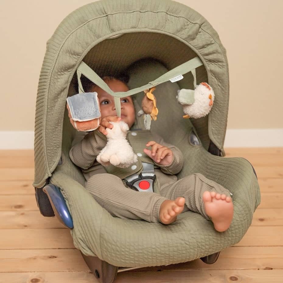 Baby spielt mit buntem Spielzeug für Kinderwagen und Autositze im komfortablen Autositz zu Hause