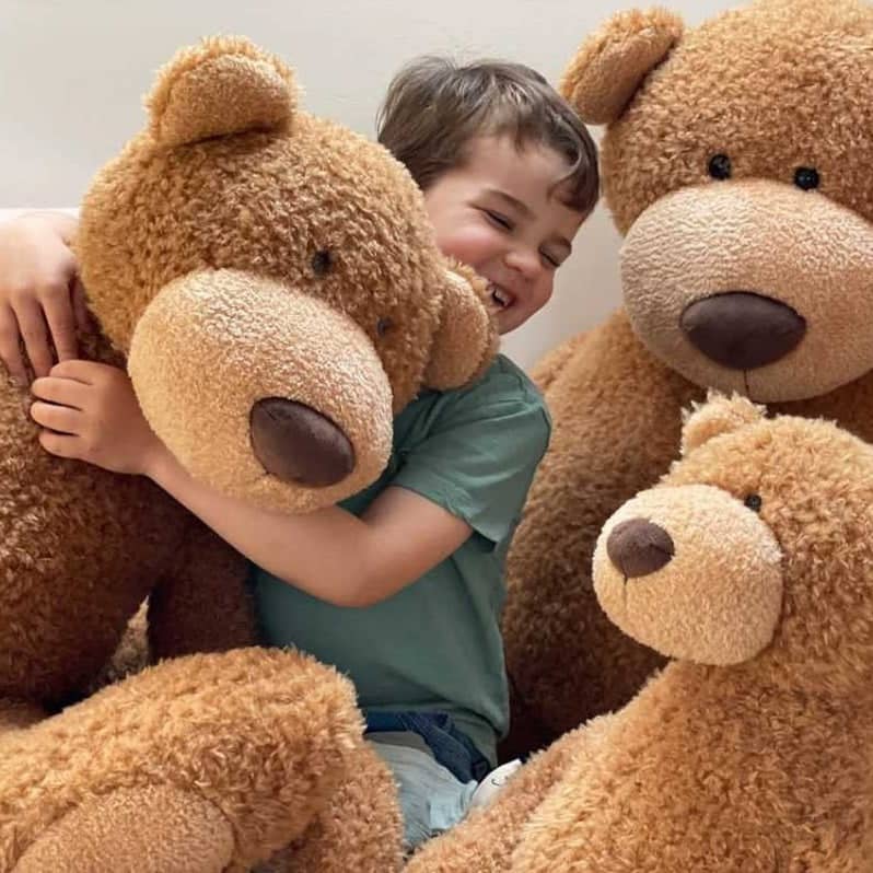 Kind umarmt große braune Stofftiere und Kuscheltiere in Form von Teddybären glücklich