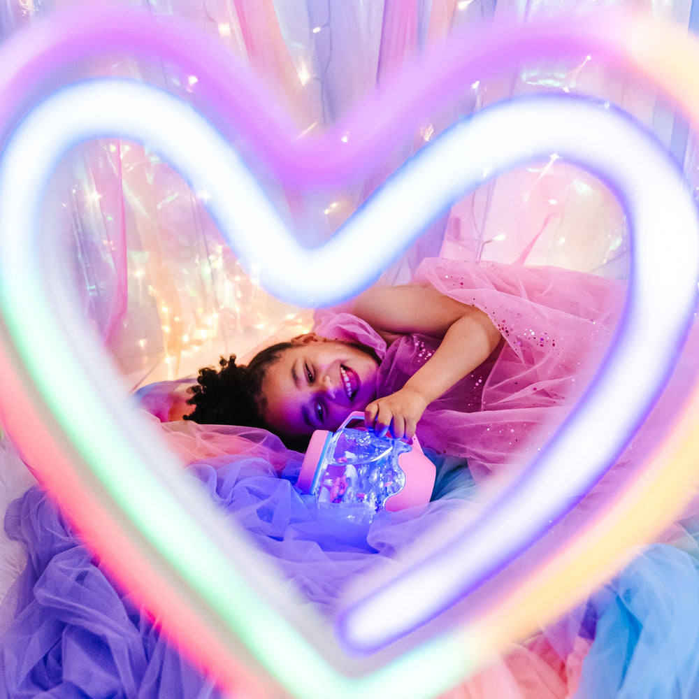 Mädchen spielt mit dem Sensorikglas zum Befüllen mit Wasser – rosa von Glo Pals in einem leuchtenden Zimmer