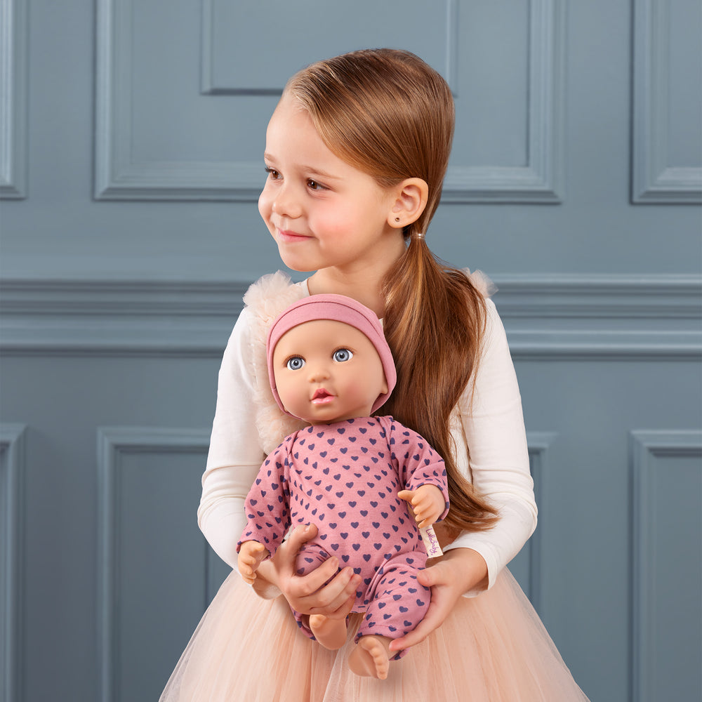 Babypuppe mit Schnuller im Pyjama mit lila Herzchen und Mütze