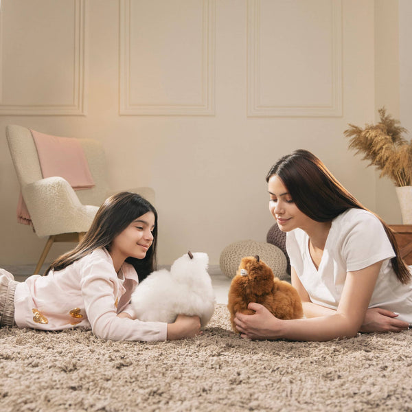 Mutter und Tochter spielen auf dem Teppich mit Alpaka-Kuscheltieren