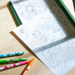 Abgepauste Cozy-Zeichnung auf Papier neben bunten Neon-Kreidemarkern