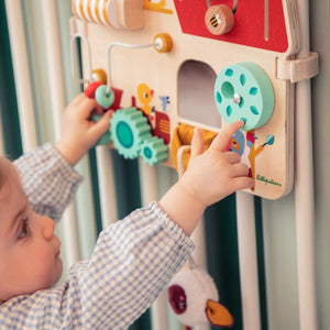 Baby spielt mit dem Activity-Board Bauernhof am Babybett