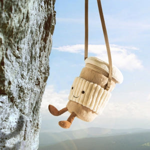 Jellycat Coffee-to-go-Tasche hängt am Riemen vor Himmel und Felsen