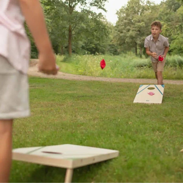 Zwei Kinder spielen Wurfspiel aus Holz auf einem grünen Spielplatz im Freien