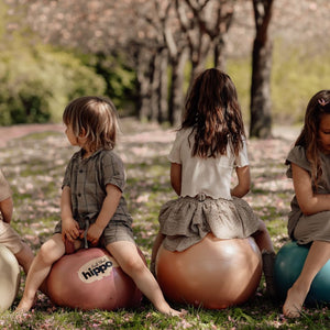 Kinder spielen draußen auf Hüpfball Rosa von Find that Hippo im Garten unter blühenden Bäumen