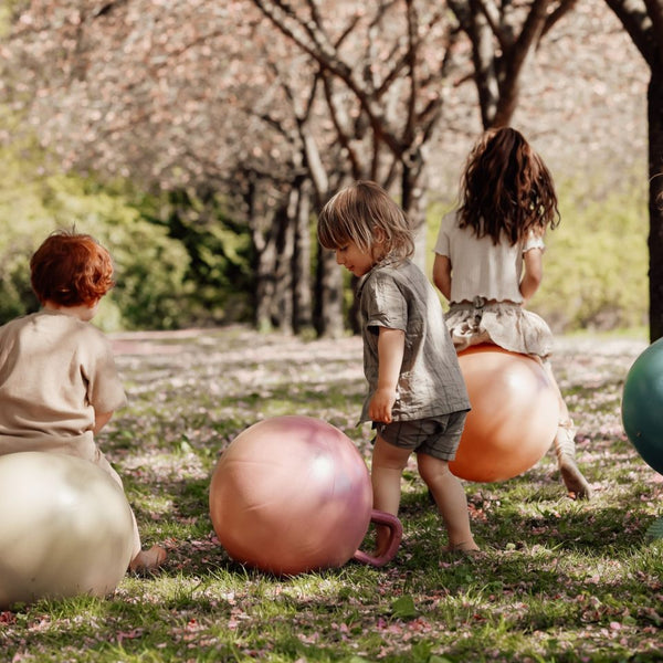 Drei Kinder spielen draußen mit bunten Hüpfball Rosa und anderen Hüpfbällen im Park