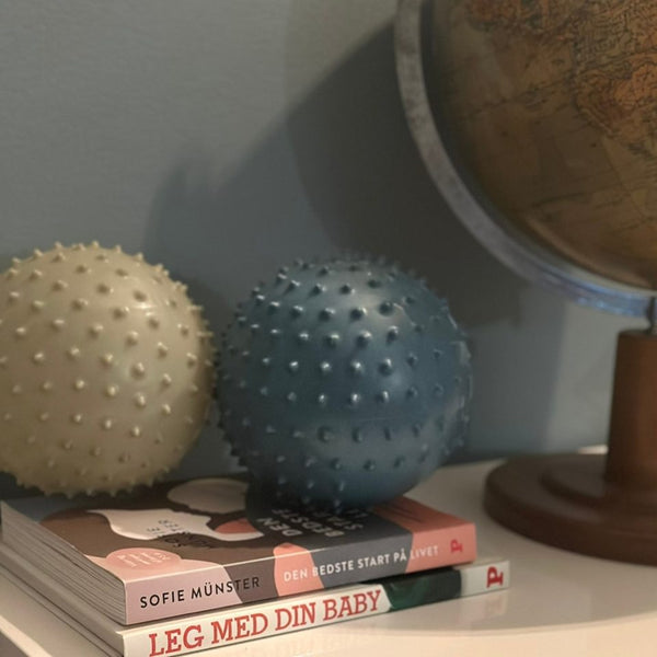 Sensorikbälle 2 Stück Sea von Find that Hippo, zwei stachelige Massagebälle in Beige und Blau auf Büchern neben Globus