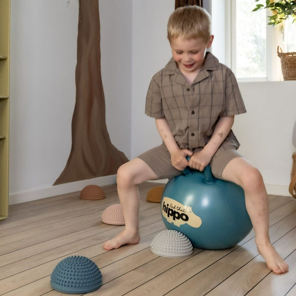 Kind sitzt auf einem blauen Hüpfball Blau von Find that Hippo in einem hellen Raum