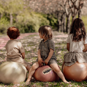 Drei Kinder sitzen draußen auf bunten Find that Hippo Hüpfball Grün und anderen Hüpfbällen im Park