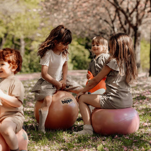 Kinder spielen draußen auf einem Hüpfball Orange von Find that Hippo im Park bei Sonnenschein