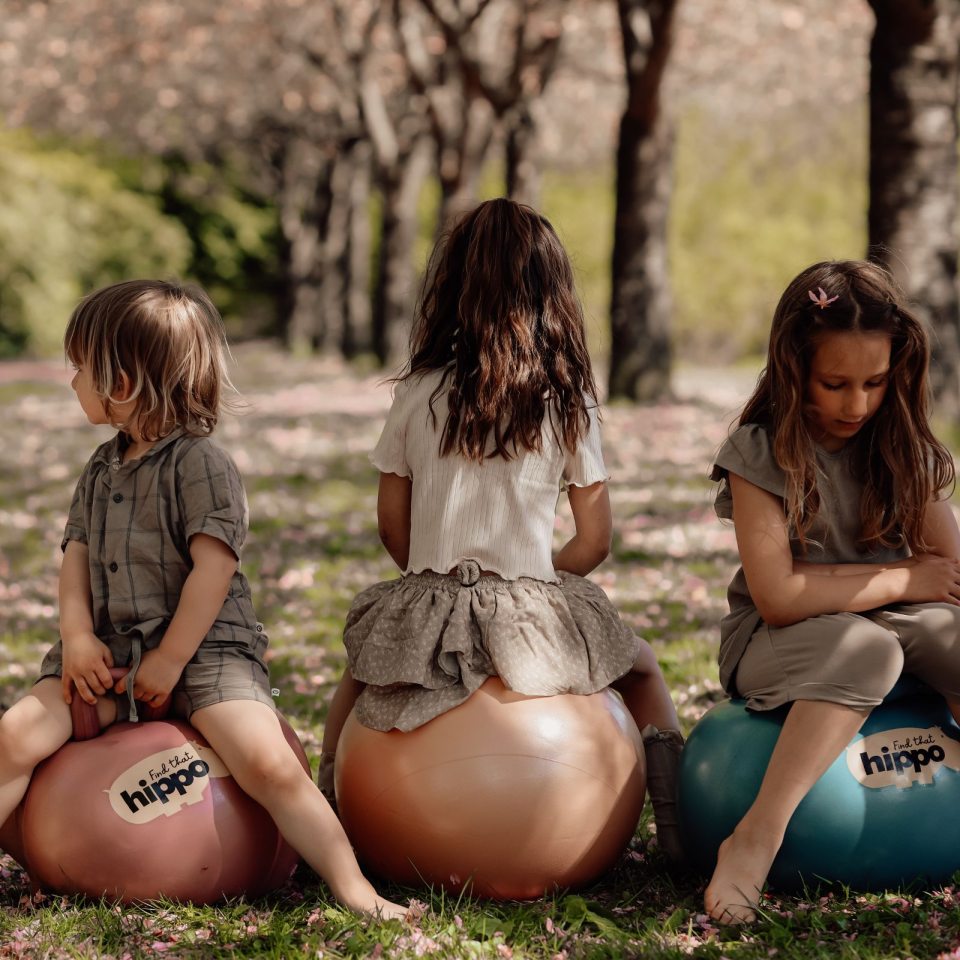 Mädchen sitzt draußen auf einem orangefarbenen Hüpfball Orange von Find that Hippo im Park