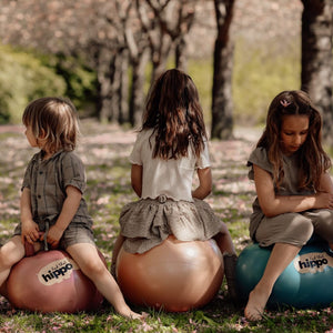 Drei Kinder sitzen auf Hüpfball Orange und anderen Farben von Find that Hippo im Park