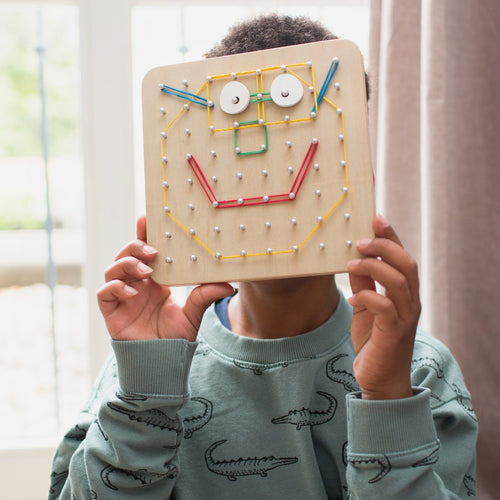 Kind hält Holz Geoboard für Kinder mit bunten Stiften und Gesichtsdesign in den Händen