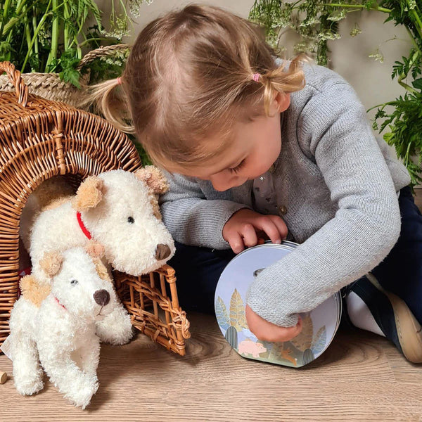 Ein Mädchen spielt mit zwei Egmont Toys Kuschelhund Eliot klein aus weichem Material neben einem Korbhäuschen