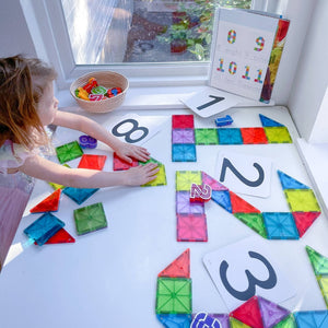 Kind spielt mit Magnetbausteinen Kinder von MAGNA-TILES auf einem Tisch mit Zahlen und Formen