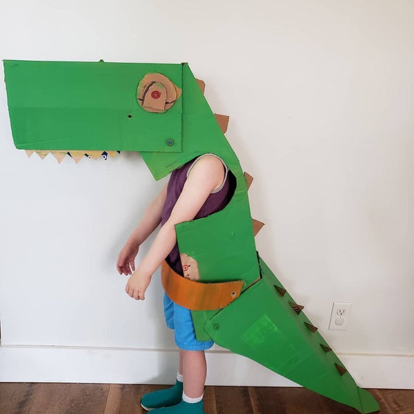 Kind trägt einen grünen Dinosaurierkostüm aus Karton mit Makedo Werkzeugen und sicherer Kartonperforierroller Fold-Roller