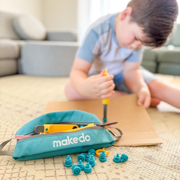 Makedo Tasche für Werkzeuge und Schrauben mit gelbem Werkzeug und blauen Schrauben vor spielendem Kind