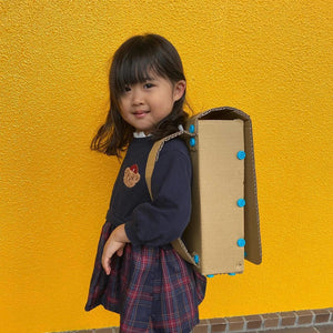 Kind mit selbstgebautem Rucksack aus Pappe als Werkzeugsatz für DIY-Konstruktionen von Makedo