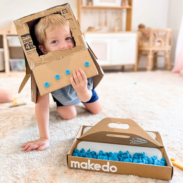 Junge spielt mit Makedo Werkzeugsatz für DIY-Konstruktionen aus Pappe in einem hellen Raum