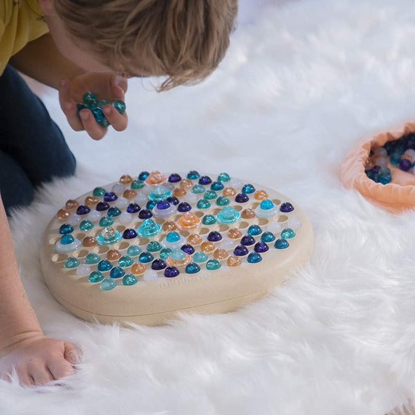 Kind spielt mit Miniland Puzzle – Mandala-Stein Holzpuzzle mit bunten Glassteinen auf weißem Teppich