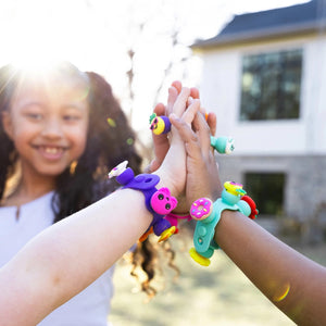 Kinder mit bunten Armbändern aus dem Schmuckset Plip Charms – Rosa beim gemeinsamen Spielen draußen