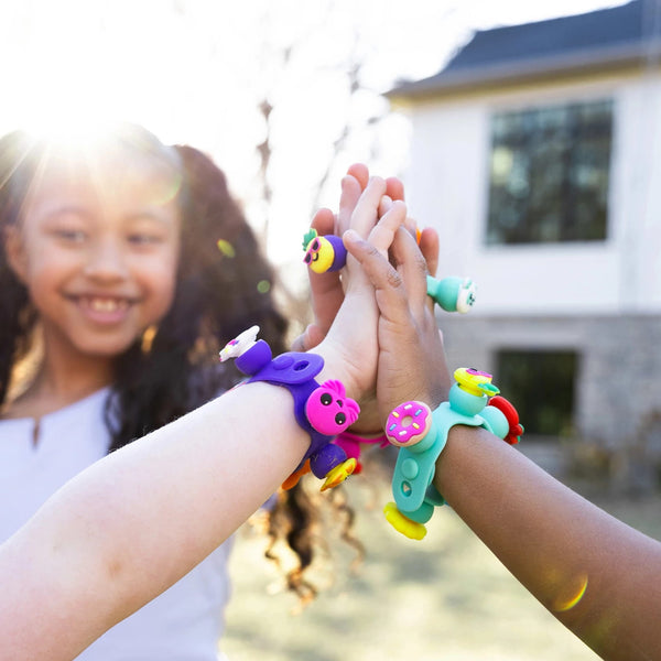 Kinder mit bunten Armbändern aus dem Schmuckset Plip Charms – Rosa beim gemeinsamen Spielen draußen
