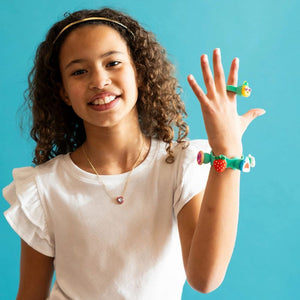 Mädchen trägt Schmuckset Plip Charms – Violett von Fat Brain Toys mit buntem Armschmuck und Ring