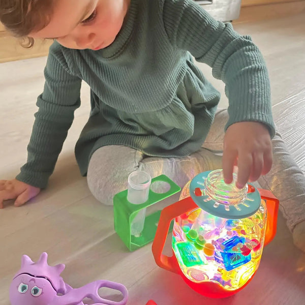 Kind spielt mit der Zabawka progresywna von Glo Pals und Sensorik-Glas zum Befüllen mit Wasser – rot