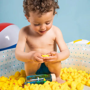 Ein Kleinkind spielt mit einer Sensorikflasche für Kinder in einem Pool voller gelber Gummienten