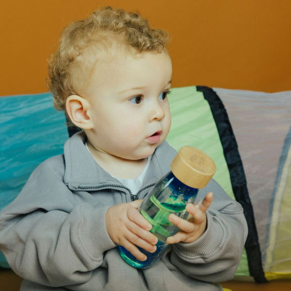 Kleines Kind mit Sinnesflasche für Kinder aus Holz und buntem Wasser für sensorische Spiele