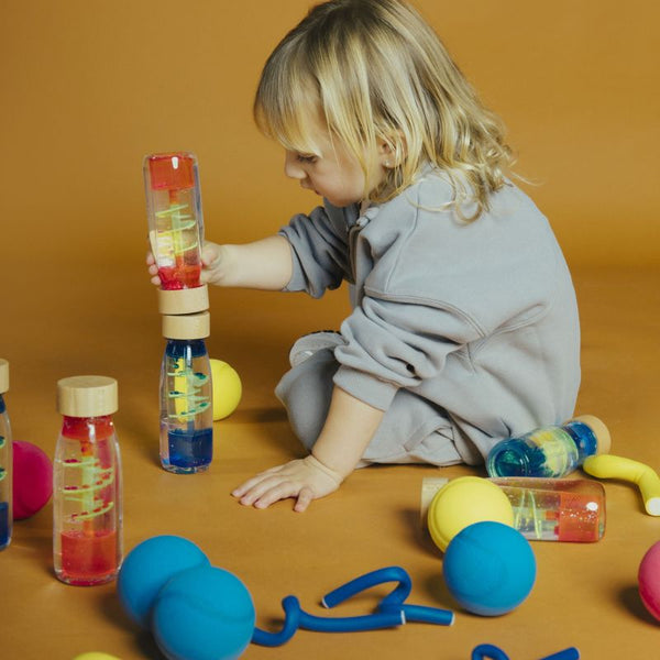 Kleines Kind, das mit bunter Sinnesflasche für Kinder von Petit Boum spielt und die Flaschen stapelt
