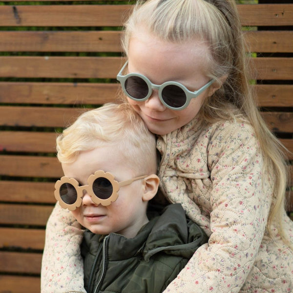 Kind mit Sonnenbrille Craspedia – Blush Rose 3–8 Jahre im Arm eines älteren Kindes vor Holzwand
