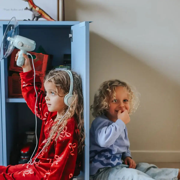 Zwei Kinder mit einem Soundverstärker für Kinder, eines mit Kopfhörern und das andere lächelnd daneben