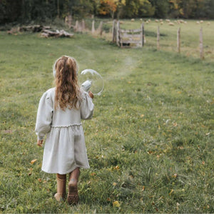 Mädchen in einem weißen Kleid mit Soundverstärker für Kinder in der Hand, das auf einem grünen Feld läuft.