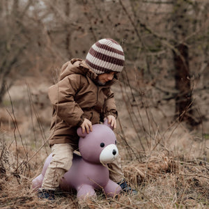 Kind sitzt draußen auf einem lila Springer Bär Spielzeug von Find that Hippo