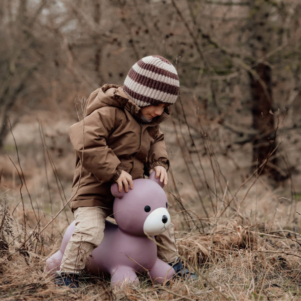 Kind sitzt draußen auf einem lila Springer Bär Spielzeug von Find that Hippo