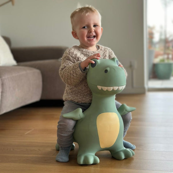 Kleinkind sitzt auf grünem Springer Dinosaurier Spielzeug von Find that Hippo im Wohnzimmer