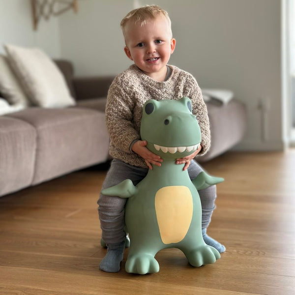 Kleinkind sitzt auf grünem Springer Dinosaurier Skoczek von Find that Hippo im Wohnzimmer
